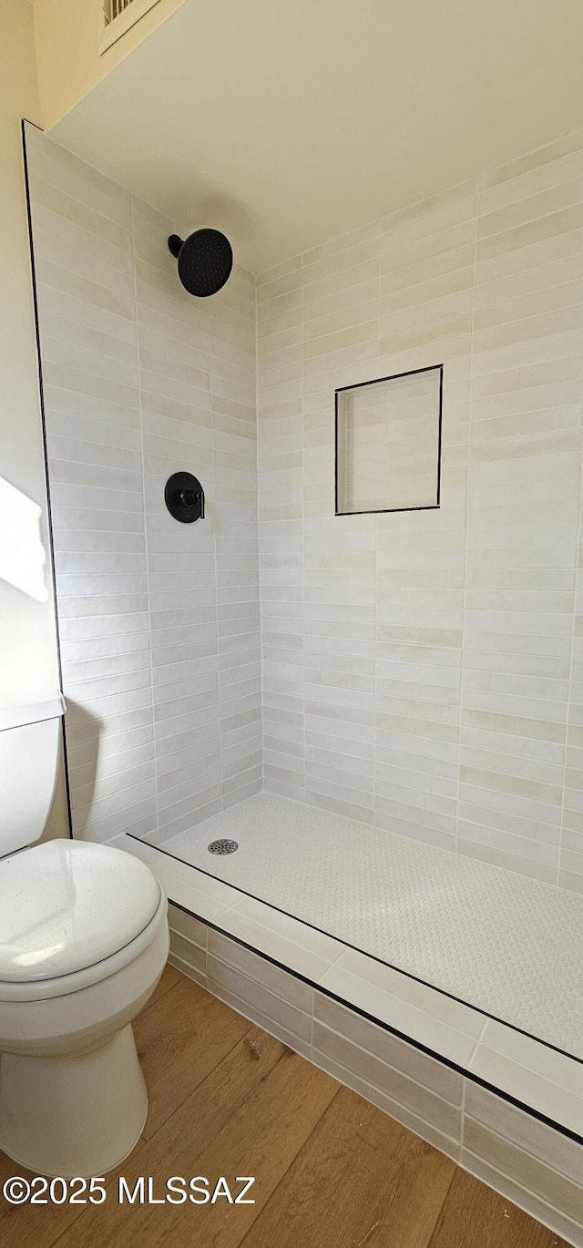 bathroom featuring wood-type flooring, a tile shower, and toilet