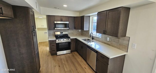 kitchen with sink, appliances with stainless steel finishes, dark brown cabinetry, decorative backsplash, and light wood-type flooring