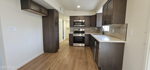 kitchen featuring appliances with stainless steel finishes, sink, backsplash, dark brown cabinetry, and light hardwood / wood-style flooring