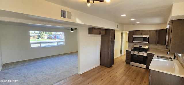 kitchen with sink, stainless steel appliances, tasteful backsplash, dark brown cabinetry, and light colored carpet