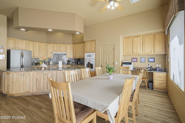 dining space featuring ceiling fan, visible vents, light wood-style flooring, and a towering ceiling