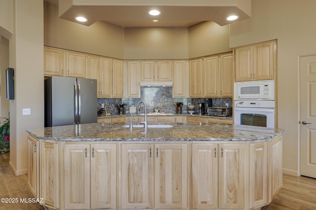 kitchen featuring decorative backsplash, white appliances, under cabinet range hood, and light brown cabinetry