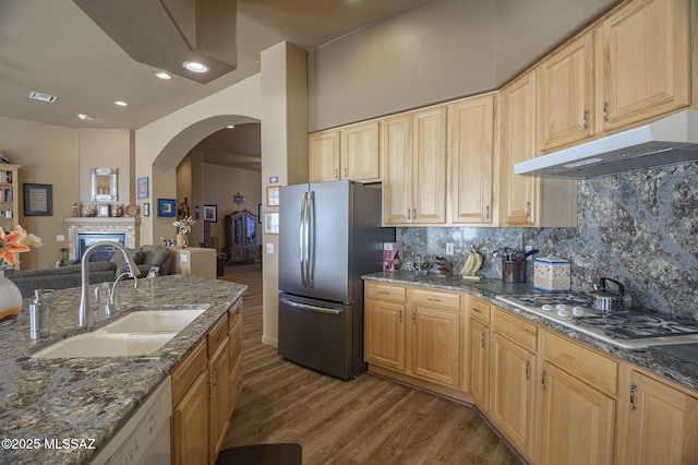 kitchen with under cabinet range hood, a sink, backsplash, wood finished floors, and white appliances