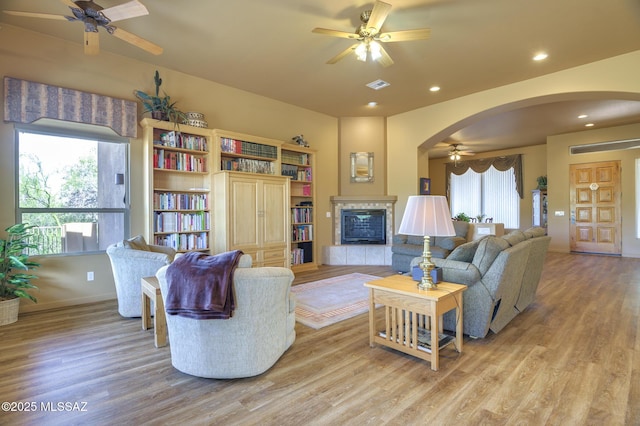 living area featuring arched walkways, a fireplace, and ceiling fan