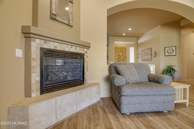 living room with baseboards, recessed lighting, a tile fireplace, wood finished floors, and arched walkways