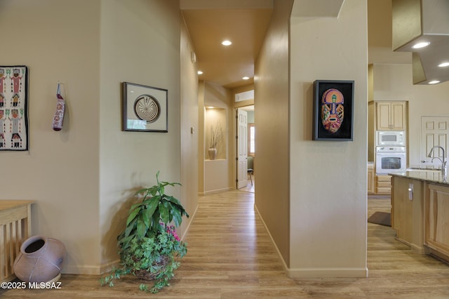 hall featuring recessed lighting, light wood-style flooring, baseboards, and a sink