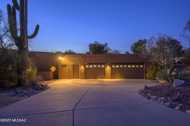 adobe home with stucco siding, an attached garage, and driveway