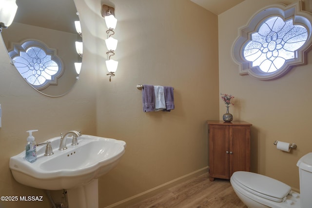 half bath with a sink, baseboards, toilet, and wood finished floors