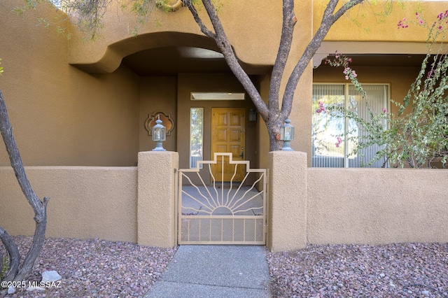 property entrance with a gate, stucco siding, and fence