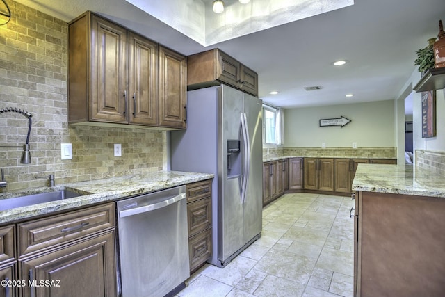 kitchen with stainless steel appliances, light stone countertops, sink, and decorative backsplash