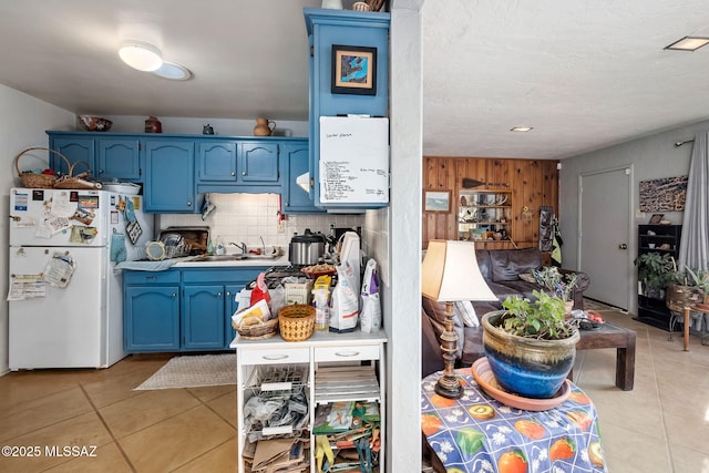 kitchen with blue cabinets, sink, light tile patterned floors, wooden walls, and white fridge