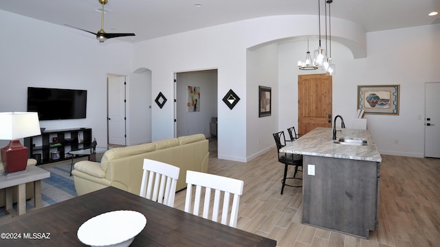 dining space featuring ceiling fan with notable chandelier, lofted ceiling, sink, and light wood-type flooring