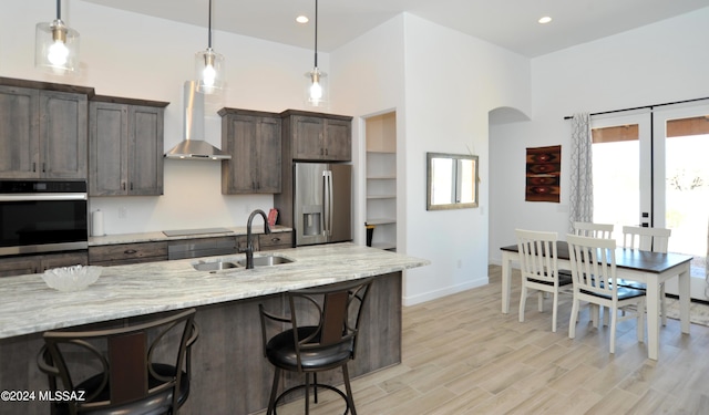 kitchen featuring stainless steel appliances, light stone countertops, sink, and wall chimney range hood