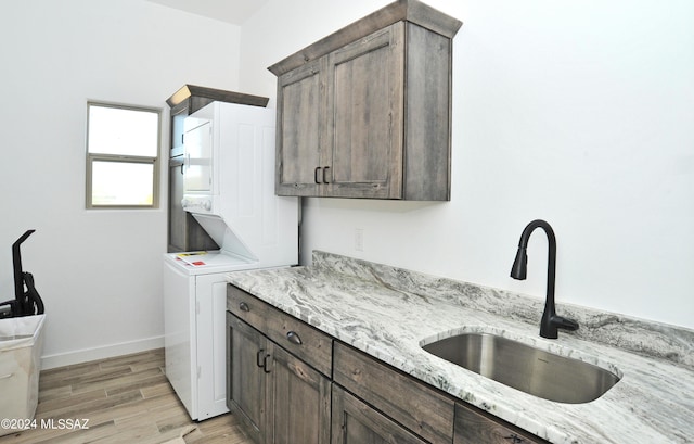 laundry room featuring cabinets, stacked washer and clothes dryer, light hardwood / wood-style floors, and sink