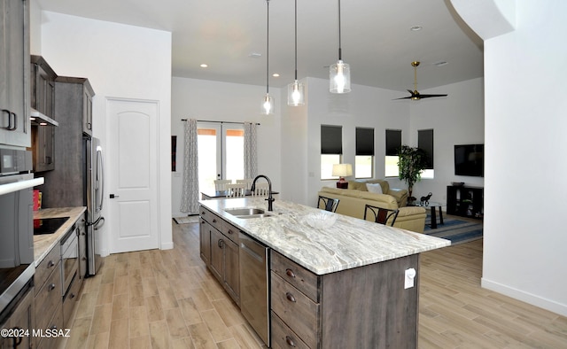 kitchen with sink, hanging light fixtures, a kitchen island with sink, light stone counters, and stainless steel appliances