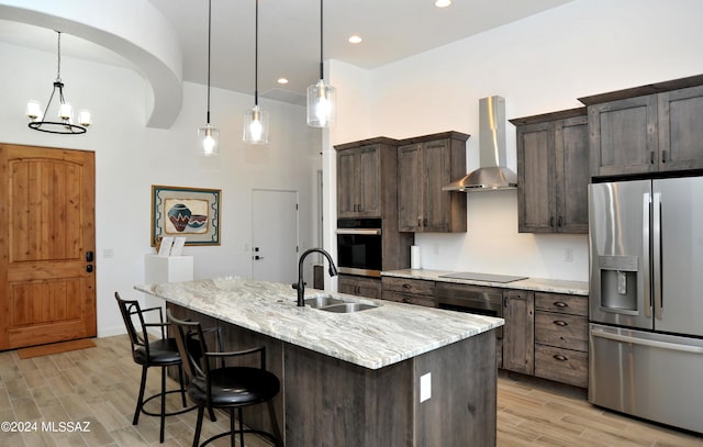 kitchen featuring light stone counters, stainless steel fridge with ice dispenser, an island with sink, oven, and wall chimney range hood