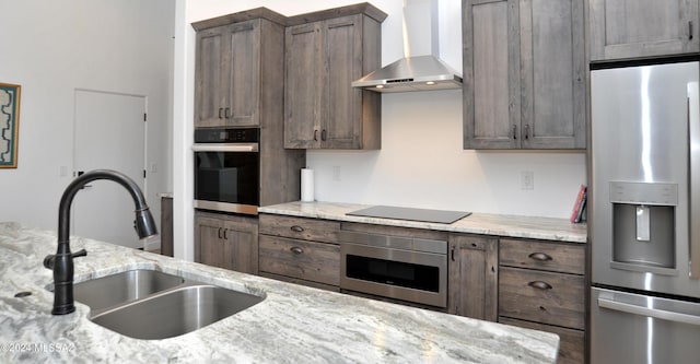 kitchen featuring light stone counters, wall chimney range hood, sink, and appliances with stainless steel finishes