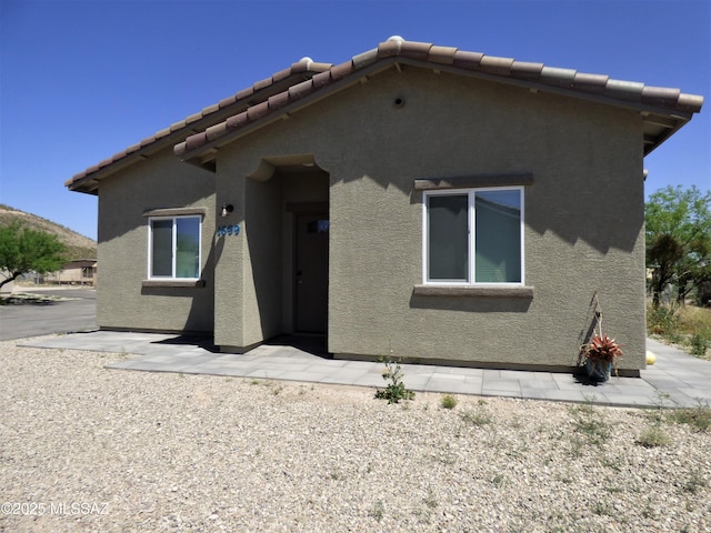 rear view of property with a patio area, a tile roof, and stucco siding