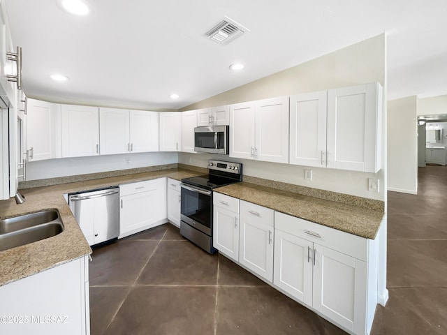 kitchen with sink, white cabinetry, light stone counters, vaulted ceiling, and appliances with stainless steel finishes