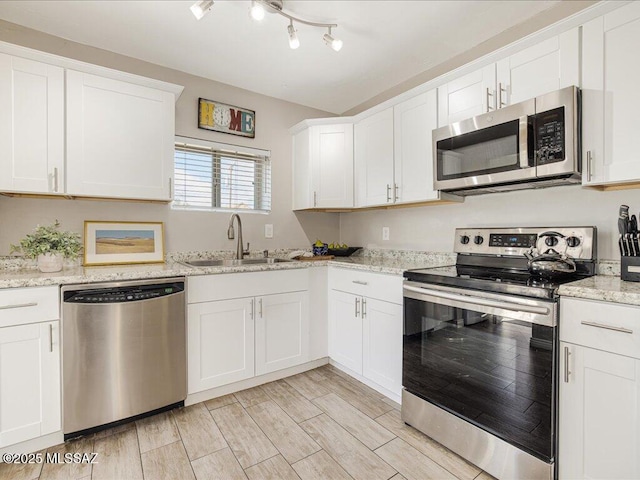 kitchen with white cabinetry, sink, light stone counters, and appliances with stainless steel finishes