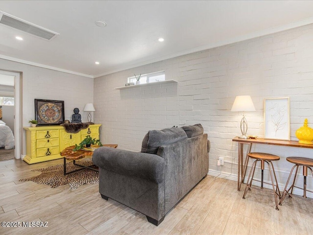 living room featuring crown molding, brick wall, light hardwood / wood-style flooring, and a wealth of natural light