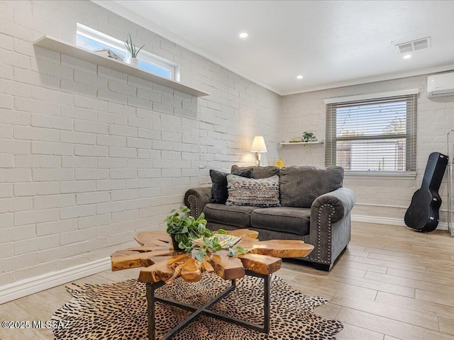 living room featuring a wall unit AC, brick wall, and light wood-type flooring