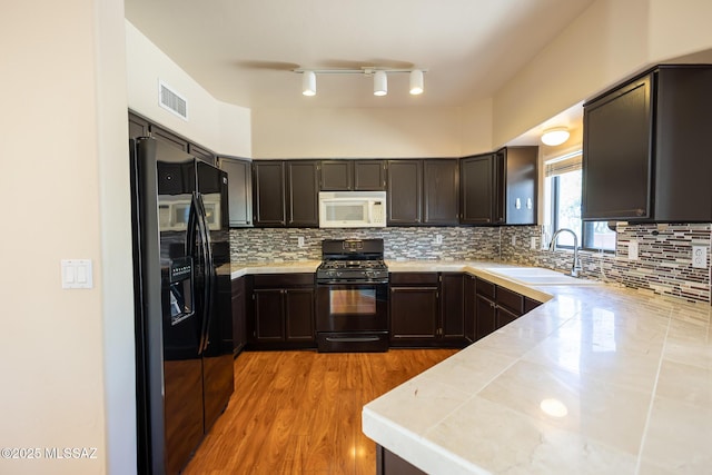 kitchen with tasteful backsplash, sink, black appliances, and light wood-type flooring