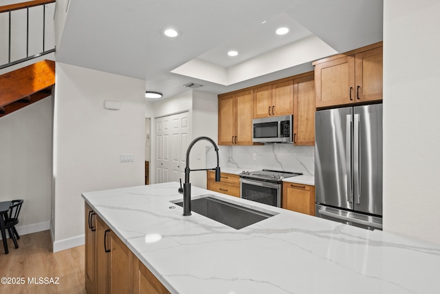 kitchen featuring sink, light stone counters, light hardwood / wood-style flooring, appliances with stainless steel finishes, and backsplash