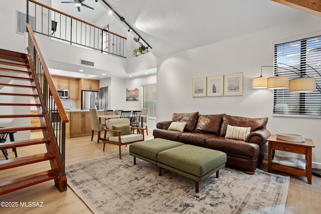 living room featuring a high ceiling, ceiling fan, and light wood-type flooring