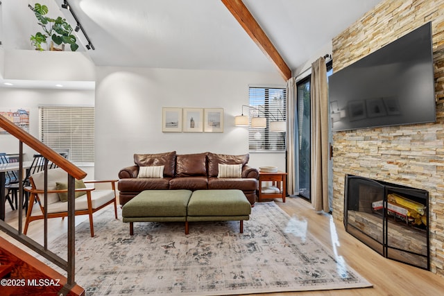 living room featuring a stone fireplace, vaulted ceiling with beams, and light hardwood / wood-style flooring