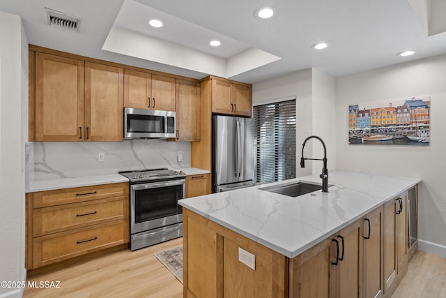 kitchen with appliances with stainless steel finishes, sink, backsplash, light stone countertops, and light hardwood / wood-style flooring