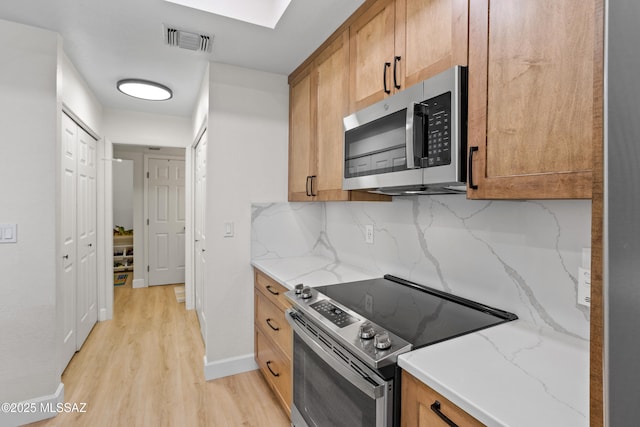 kitchen with tasteful backsplash, appliances with stainless steel finishes, light stone countertops, and light hardwood / wood-style floors