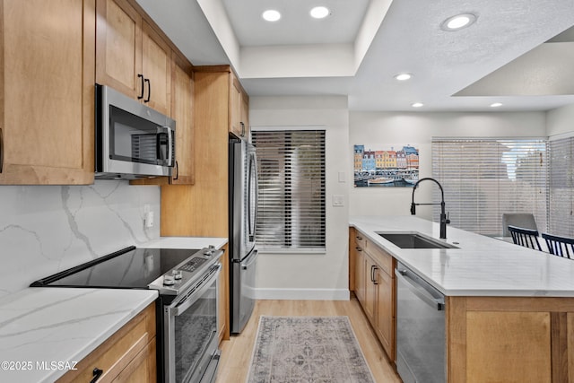 kitchen with sink, light hardwood / wood-style flooring, stainless steel appliances, light stone countertops, and backsplash