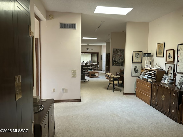 hallway with a skylight, baseboards, visible vents, and light colored carpet