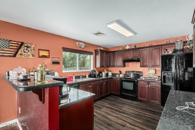 kitchen with sink, dark hardwood / wood-style floors, black appliances, a kitchen bar, and dark stone counters