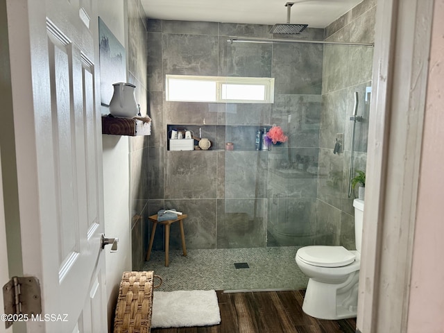 bathroom with tiled shower, wood-type flooring, and toilet