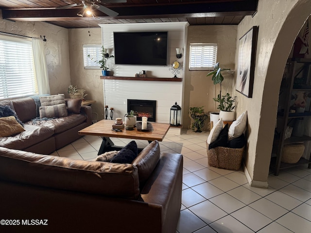 living room featuring a fireplace, a healthy amount of sunlight, beam ceiling, and light tile patterned floors