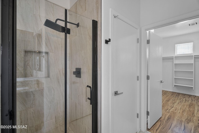 bathroom featuring a walk in closet, a shower stall, wood finished floors, and visible vents