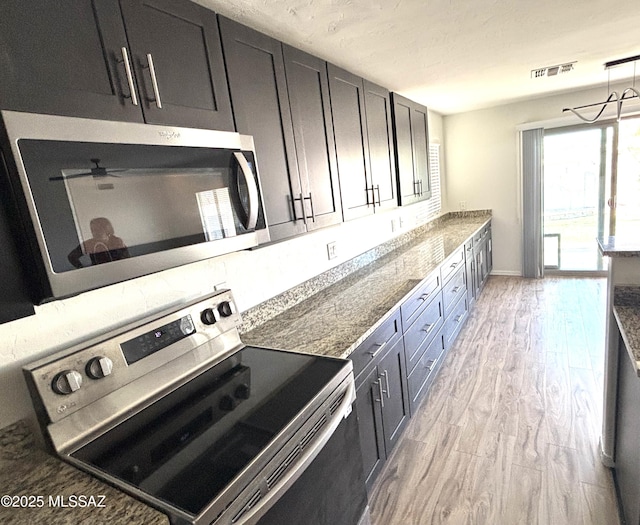 kitchen featuring decorative light fixtures, light wood-type flooring, dark stone counters, and appliances with stainless steel finishes