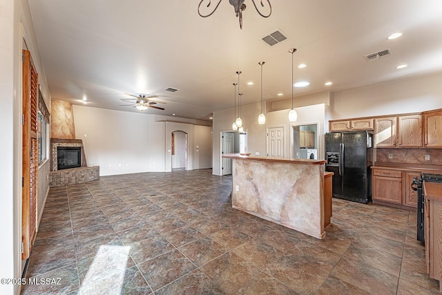 kitchen with a kitchen island, pendant lighting, range with gas stovetop, a fireplace, and black fridge with ice dispenser