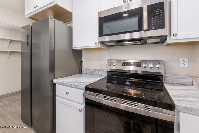 kitchen featuring stainless steel appliances, white cabinetry, light stone countertops, and light hardwood / wood-style flooring