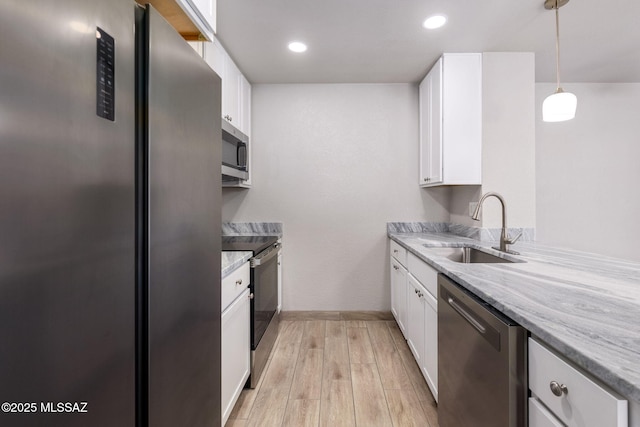 kitchen featuring stainless steel appliances, a sink, white cabinetry, light stone countertops, and pendant lighting