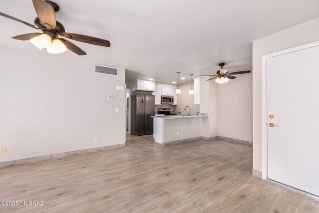 kitchen featuring white cabinetry, sink, stainless steel fridge, hanging light fixtures, and light stone counters