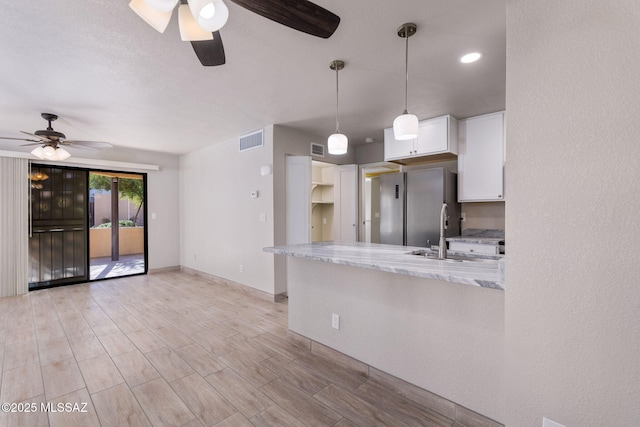 kitchen featuring light stone counters, visible vents, hanging light fixtures, white cabinets, and a sink