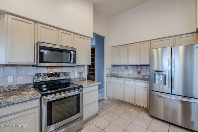 kitchen with stainless steel appliances, light stone countertops, decorative backsplash, and light tile patterned floors