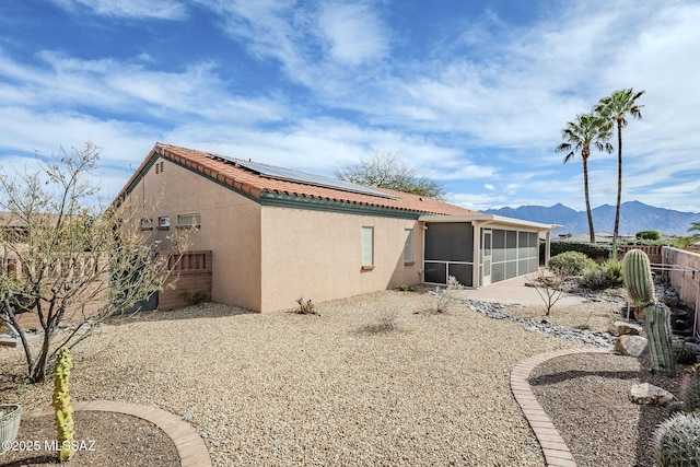 back of house with a mountain view, a sunroom, and solar panels