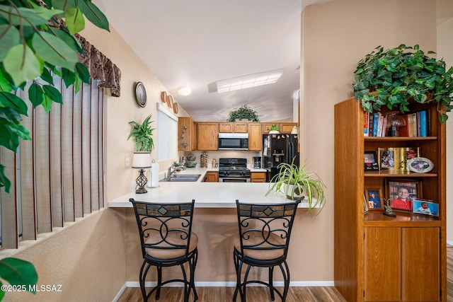 kitchen featuring stainless steel gas range, sink, a breakfast bar area, black fridge with ice dispenser, and kitchen peninsula