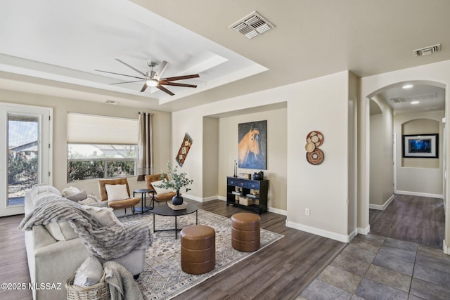 living room with dark hardwood / wood-style floors, ceiling fan, and a tray ceiling