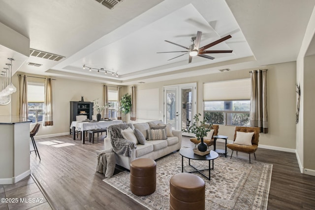 living room with a tray ceiling, dark wood-type flooring, and ceiling fan