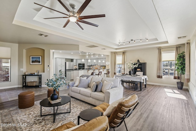 living room with ceiling fan, a tray ceiling, light hardwood / wood-style floors, and rail lighting